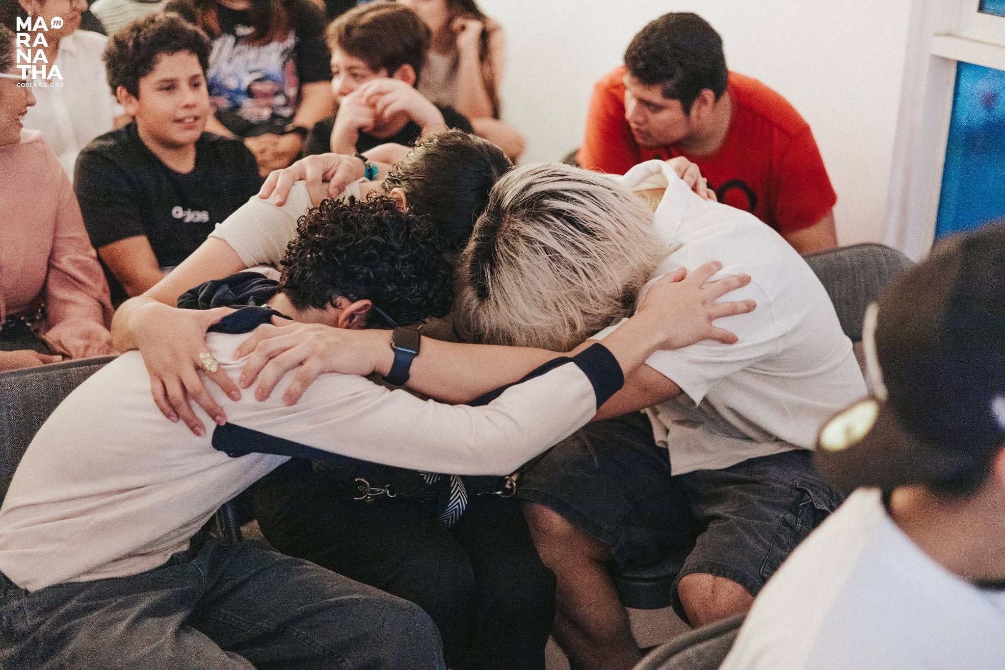 Un grupo de jóvenes abrazados orando juntos.